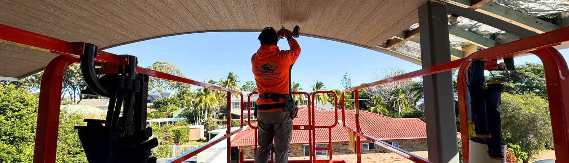 SEQ Custom Renovations tradesperson fixing timber-look ceiling lining from a lift